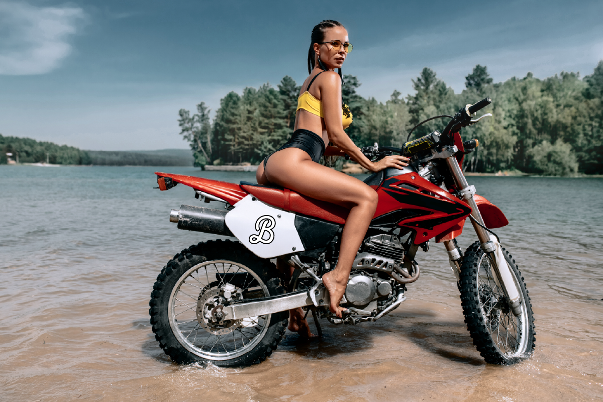 Woman sitting on a red motorcycle in shallow water near a forested area